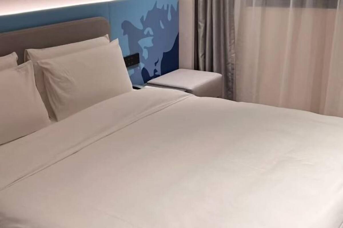 A neatly made bed with white linens, a headboard, and a bedside table with a lamp.