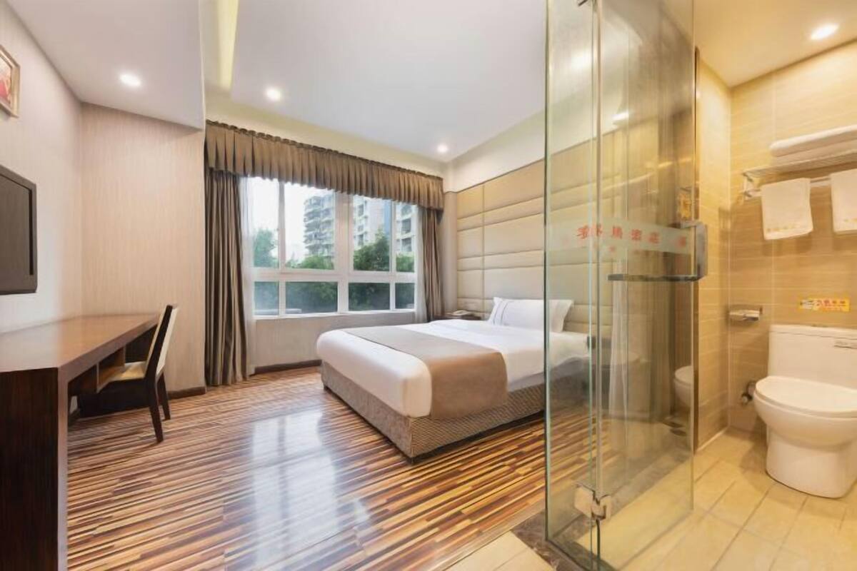 A hotel room with a bed, a desk, a chair, a shower, and a toilet.