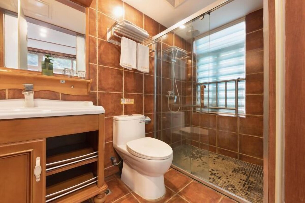A modern bathroom with a wooden vanity, a toilet, a glass shower enclosure, and a large mirror.