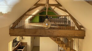 Een loft-stijl kamer met een houten plafond, een lichtslingering en uitzicht op een groene ruimte beneden.