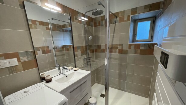 A modern bathroom with a glass shower enclosure, a built-in sink, and a small window above the mirror. - Tourangelles Stables (Bréhémont)