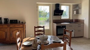 Een eetgedeelte met een houten tafel voor vier personen, een keuken met moderne apparatuur, en uitzicht op de omgeving door een glazen deur.