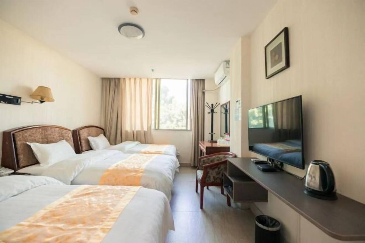 A hotel room with two beds, a desk, a television, and a window with curtains.