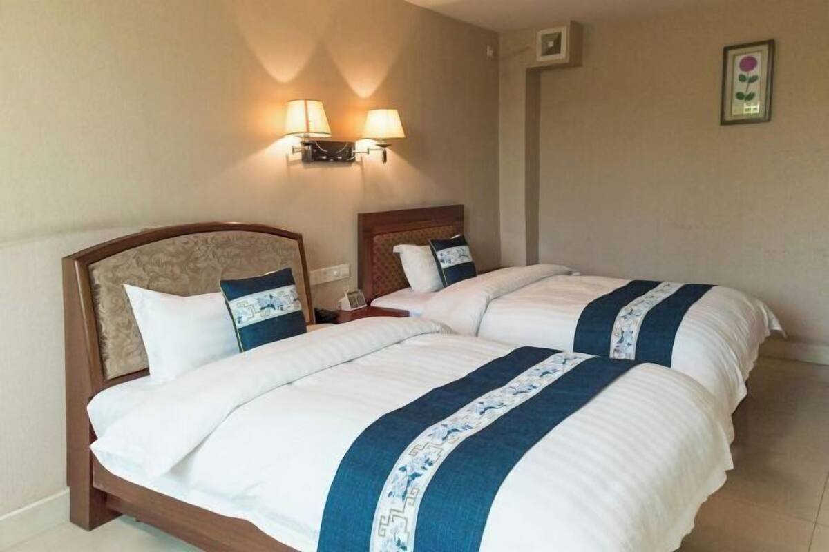 A hotel room with two beds, each with a headboard, a nightstand, and wall-mounted lamps.