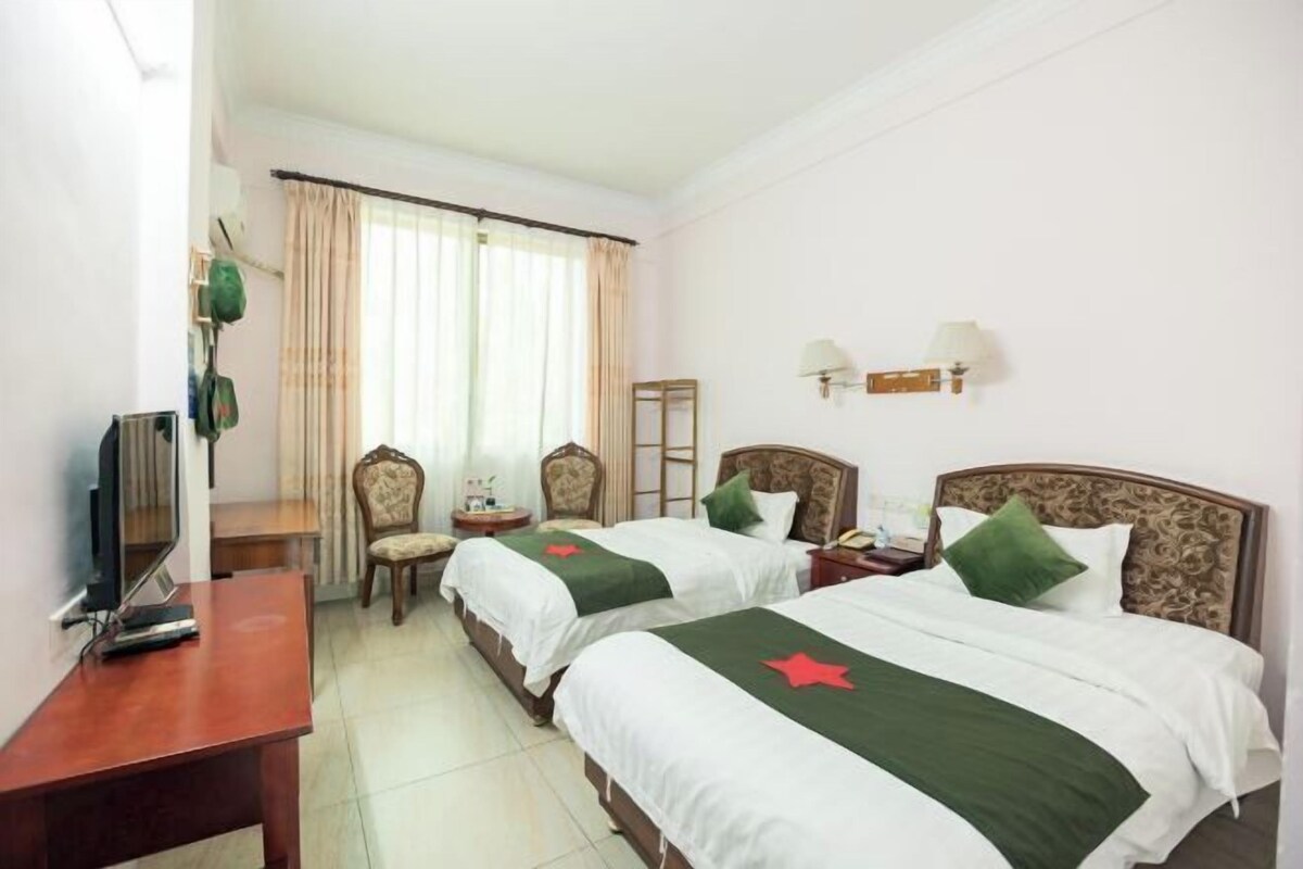 Habitación de hotel con dos camas, un escritorio, una silla, un televisor y una ventana con cortinas.