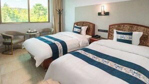 A hotel room with two beds, a small table, a chair, and a large window with a view of trees. - Yanyang Heng'an Hotel (Meizhou)