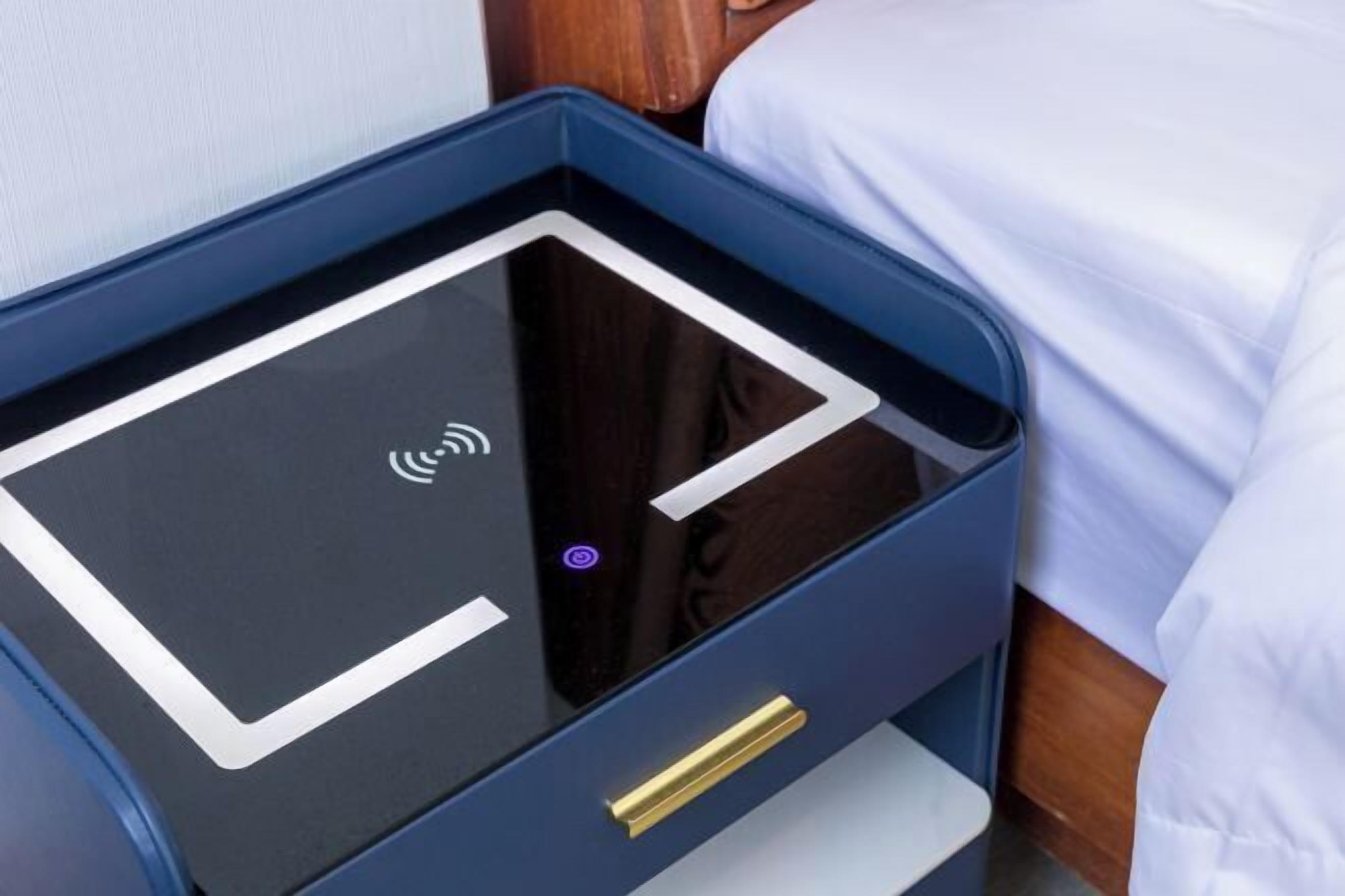 A bed with a white sheet and a bedside table with a black surface and a gold handle.