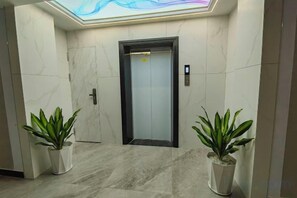 Un pasillo con piso de mármol, dos plantas en macetas y una puerta de ascensor.