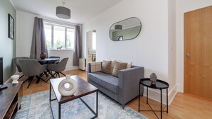 A modern living room with a grey sofa, a coffee table, and a dining area with chairs and a table. - The Hackney Apartment (London)