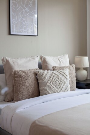 Un lit bien fait, avec une literie blanche et trois coussins décoratifs, dans une chambre d’hôtel.