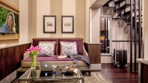 A modern living room with a sofa, a glass coffee table, and a laptop. There are framed pictures on the wall and a staircase in the background. - The Inn at the Spanish Steps Exclusive Collection - The Nest at The Spanish Steps (Rome)