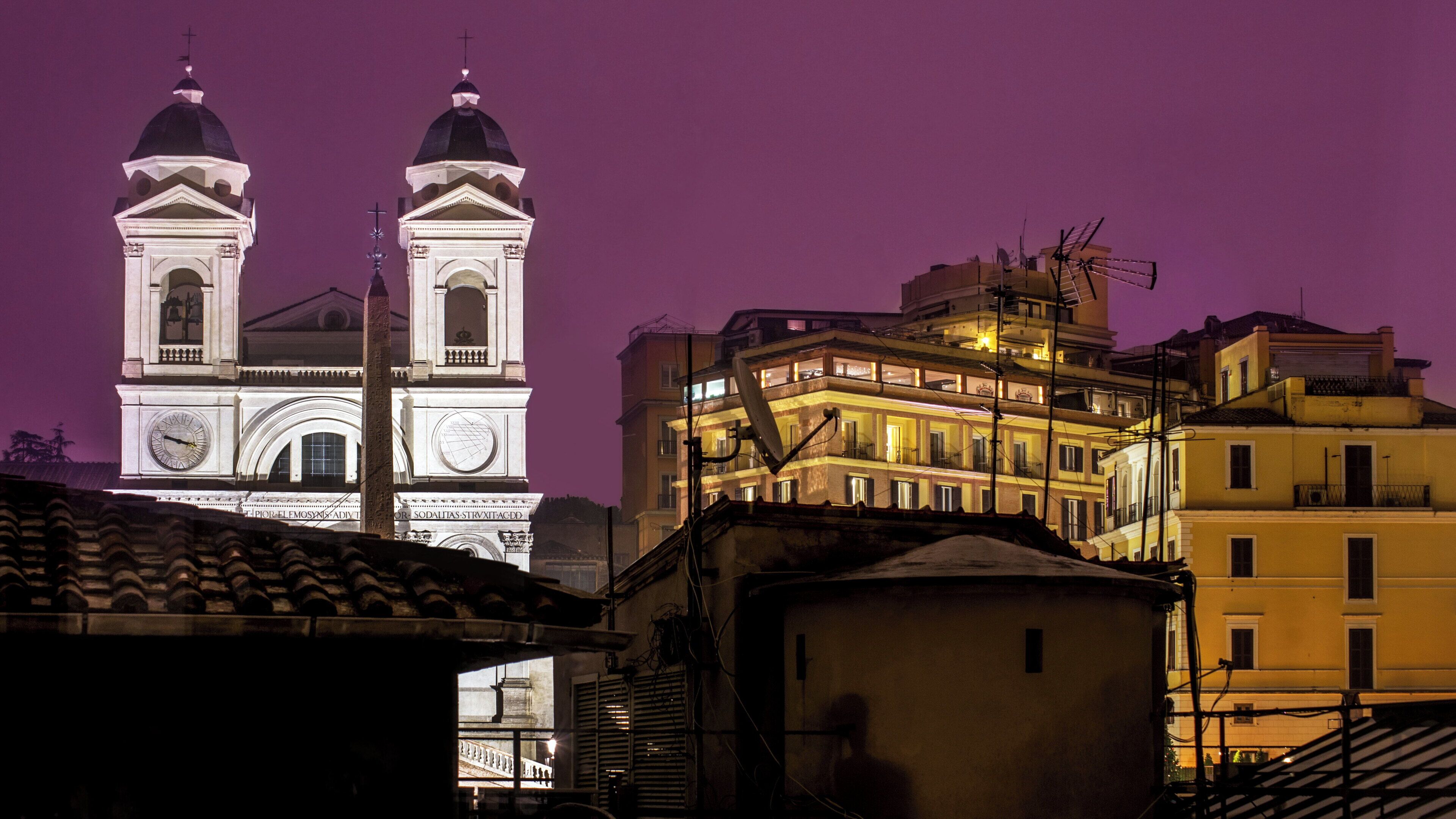 A historic building with two prominent towers, a clock, and a satellite dish.
