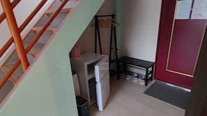 Un couloir étroit avec un escalier, une petite table avec une chaise, un réfrigérateur et un porte-manteau.