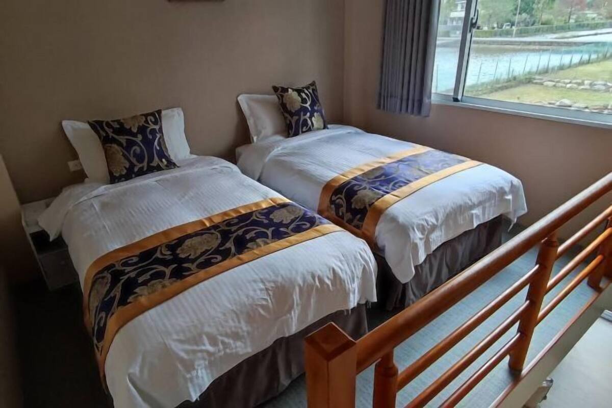 A hotel room with two beds, a wooden railing, and a window with a view of a body of water.