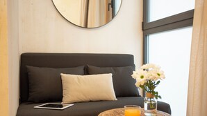 Habitación de hotel moderna con un sofá oscuro, una tableta, un vaso de zumo de naranja y un jarrón con flores blancas.
