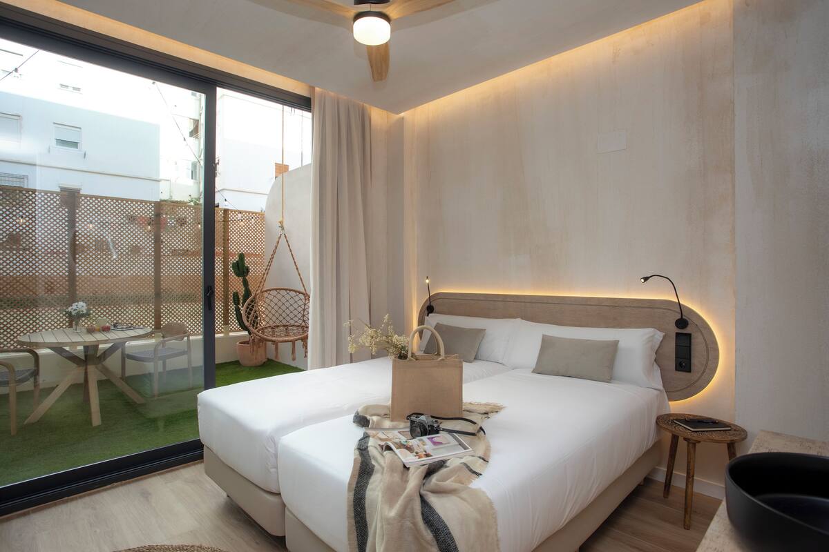 A modern hotel room with a large bed, a small side table, a chair, a dining table, and a view of the outside.