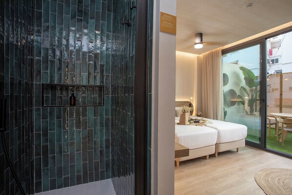 A modern hotel room with a glass door leading to a balcony, a bed, a bedside table, and a shower area with dark tiles. - Nomad Haux Mestalla (Valencia)