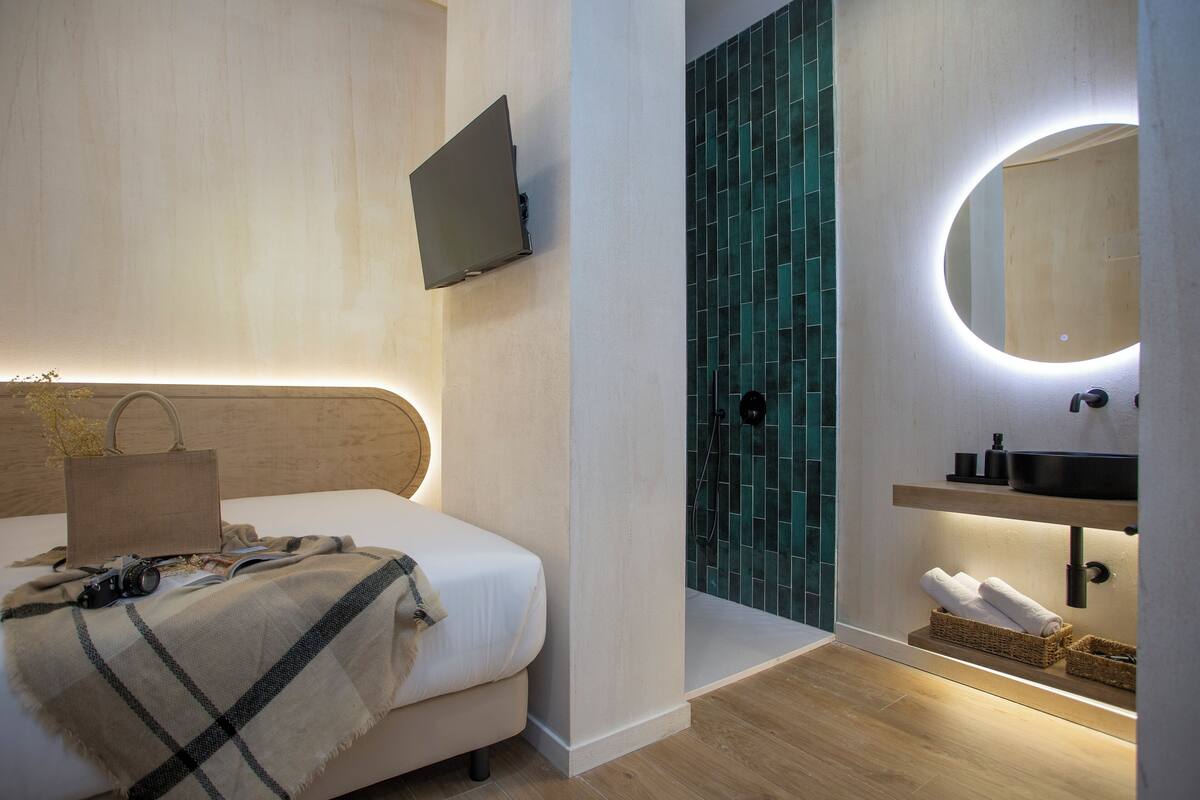 A modern bedroom with a bed, a TV, a mirror, and a bathroom with a sink and tiled walls.