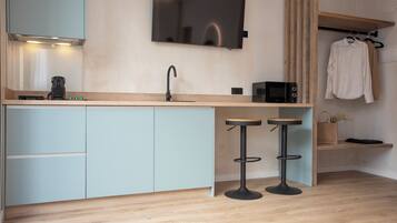 Una cocina moderna con televisor de pantalla plana, un lavamanos, cafetera, microondas y dos taburetes.