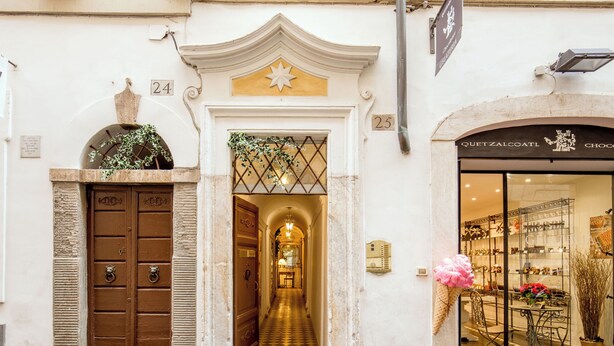 A building entrance with a checkered floor, a brown door with ornate handles, and a shop with a sign reading "QUETZALCOATL CHOCOLATE". - The Inn at the Spanish Steps Prestige Collection - The Pearl (Rome)