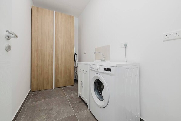 A laundry room with a washing machine, a sink, and a wooden wardrobe.