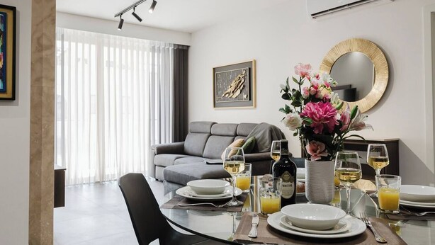 A modern living room with a grey sofa, dining table set with plates, glasses, and a bottle of wine.