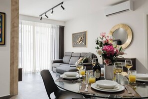 A modern living room with a grey sofa, dining table set with plates, glasses, and a bottle of wine.