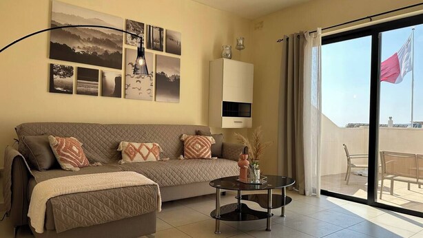 Ein modernes Wohnzimmer mit einer Couch, einem Glastisch und einem großen Fenster mit Blick ins Freie.