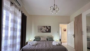 Ein Schlafzimmer mit einem großen Bett, einer Kristallleuchter, einem Gemälde an der Wand und einer Tür zu einem anderen Raum.