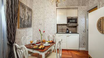 Zona pranzo con tavolo in legno, sedie bianche e un quadro raffigurante un elefante. Sullo sfondo, una cucina con mobili bianchi e una cappa in acciaio inossidabile.