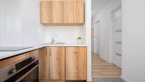 A modern kitchen with wooden cabinets, a white countertop, and a stainless steel sink. - Air-conditioned Apartment | Close to the Royal Baths (Warszawa)