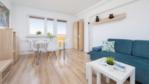 A modern living room with a blue sofa, a white coffee table, and a dining area with a white table and chairs. - Air-conditioned Apartment | Close to the Royal Baths (Warszawa)