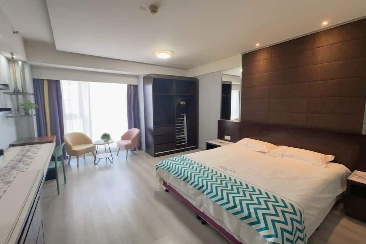 Habitación de hotel con cama, mesita de noche, silla, escritorio, armario y vistas al exterior.