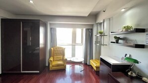 A modern room with a sliding door, a yellow armchair, a small round table, a sofa, a desk with a lamp, and shelves with plants. - City Tribe Apartment (Nanjing Kairun Jincheng) (Nanjing)