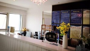 A hotel reception area with a cash register, a sign for the cashier, informational posters on the wall, and a decorative flower vase. - City Tribe Apartment (Nanjing Kairun Jincheng) (Nanjing)