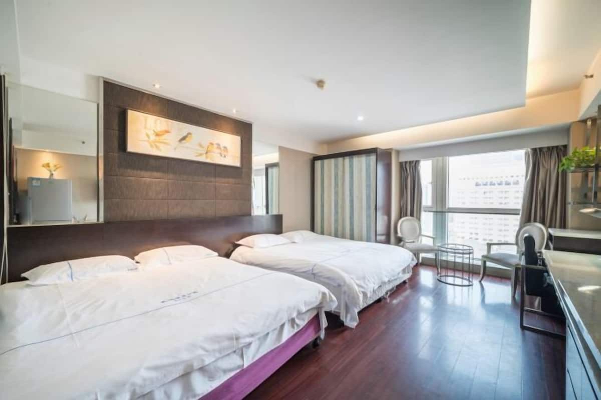 Habitación de hotel con dos camas, un ventanal grande, un cuadro en la pared y una mesita pequeña.