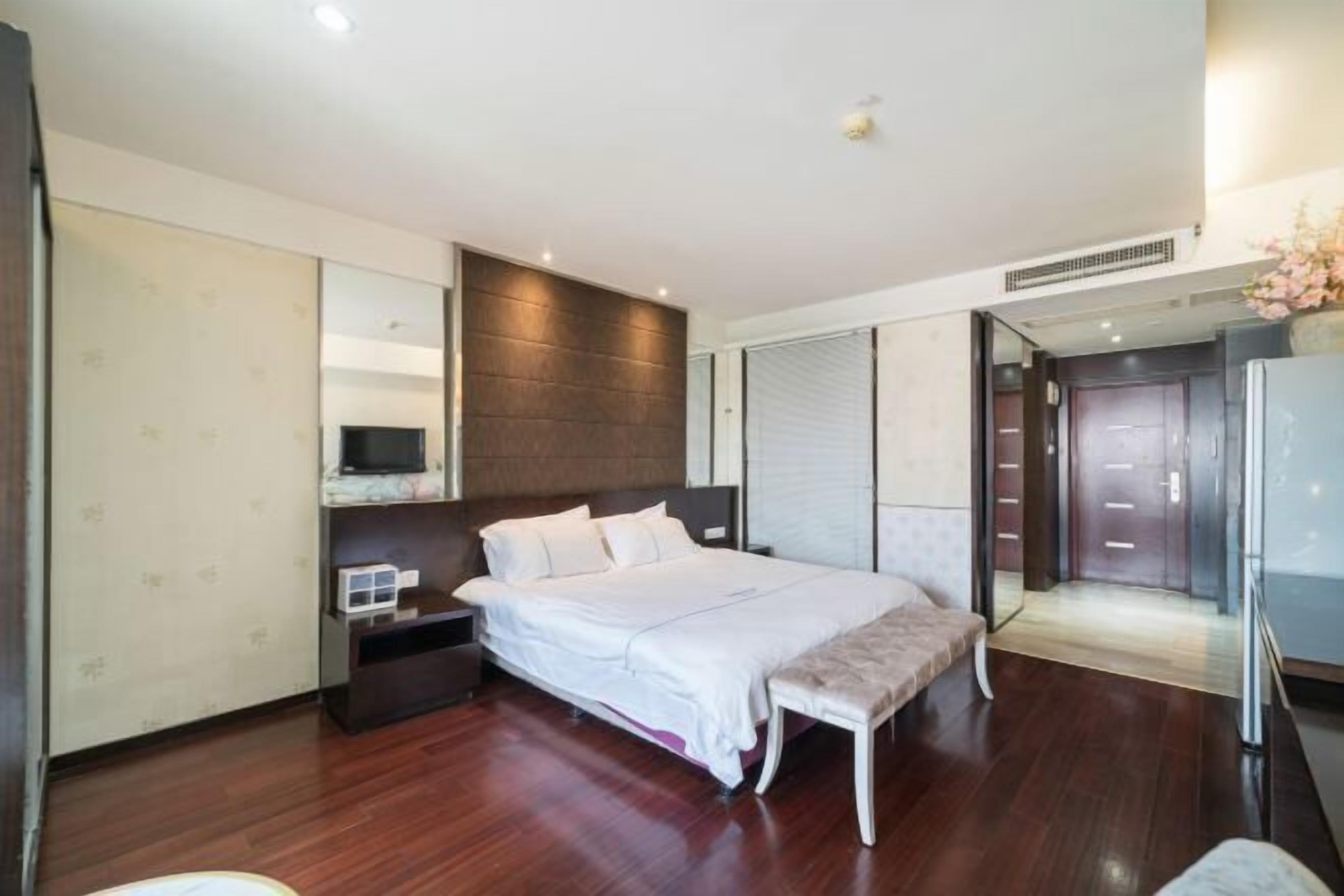 A modern bedroom with a large bed, bedside tables, a bench, and a wardrobe.