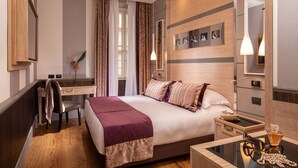 A modern hotel room with a large bed, a desk, and a mirror. There is a vase with flowers on the desk and a glass of whiskey on the nightstand. - The Inn at the Spanish Steps Luxury Collection - Mario de' Fiori Home (Rome)