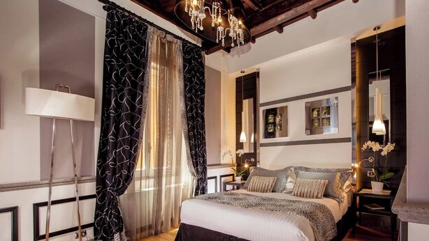 A bedroom with a large bed, a chandelier, a bedside table with a lamp, and a mirror. - The Inn at the Spanish Steps Luxury Collection - Mario de' Fiori Home (Rome)