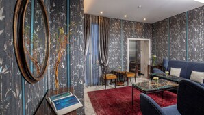 A modern living room with a red rug, a blue sofa, and a glass coffee table. - The Inn at the Spanish Steps Luxury Collection - Mario de' Fiori Home (Rome)