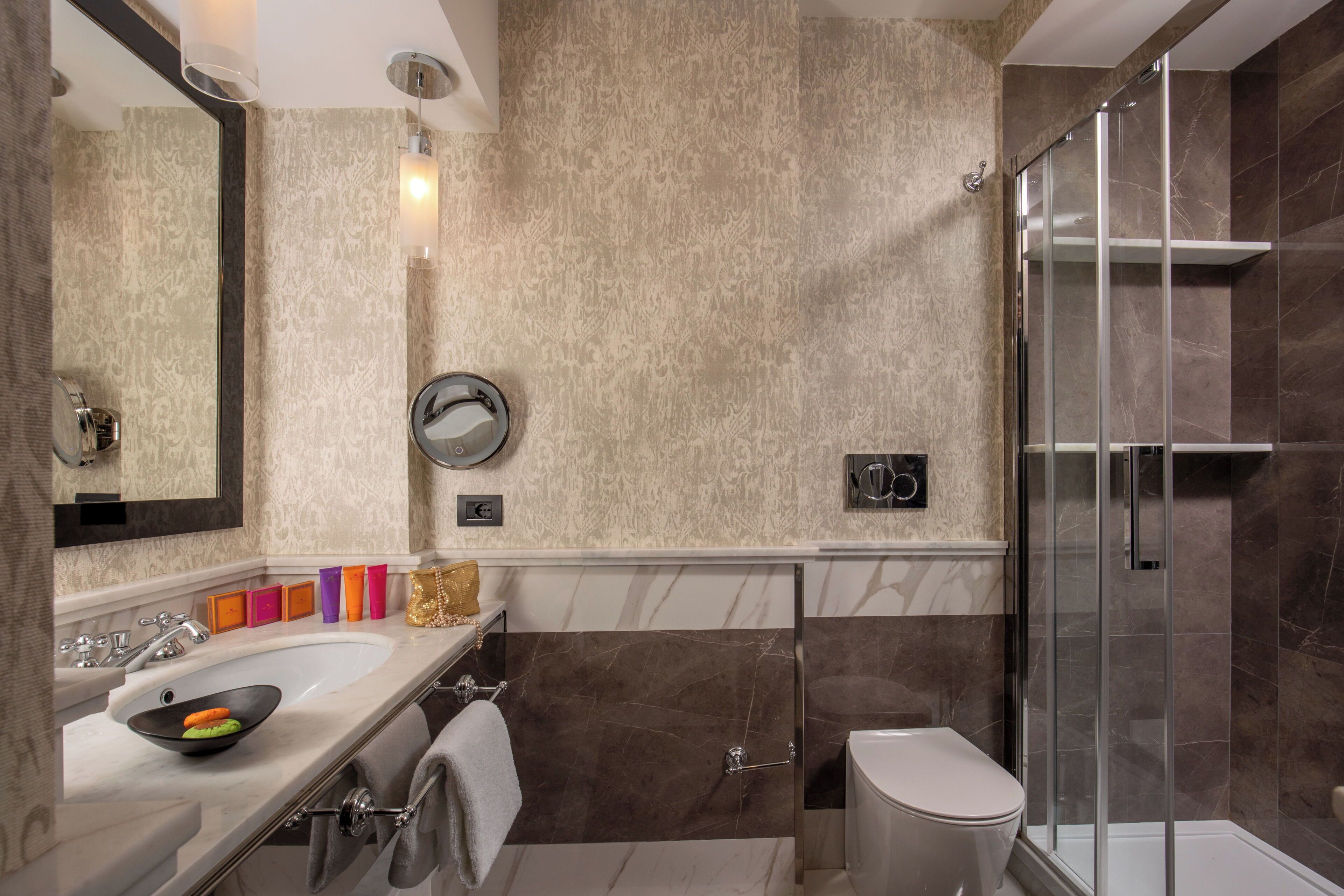 Un baño moderno con lavamanos de mármol, cabina de ducha con mampara de vidrio y retrete.