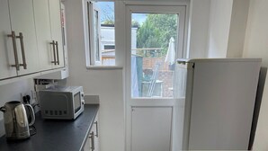 A compact kitchen with white cabinets, a black countertop, a microwave, a kettle, and a refrigerator. - 4 Beds, Sleeps 15, Near Lcy Airport & Excel London (London)