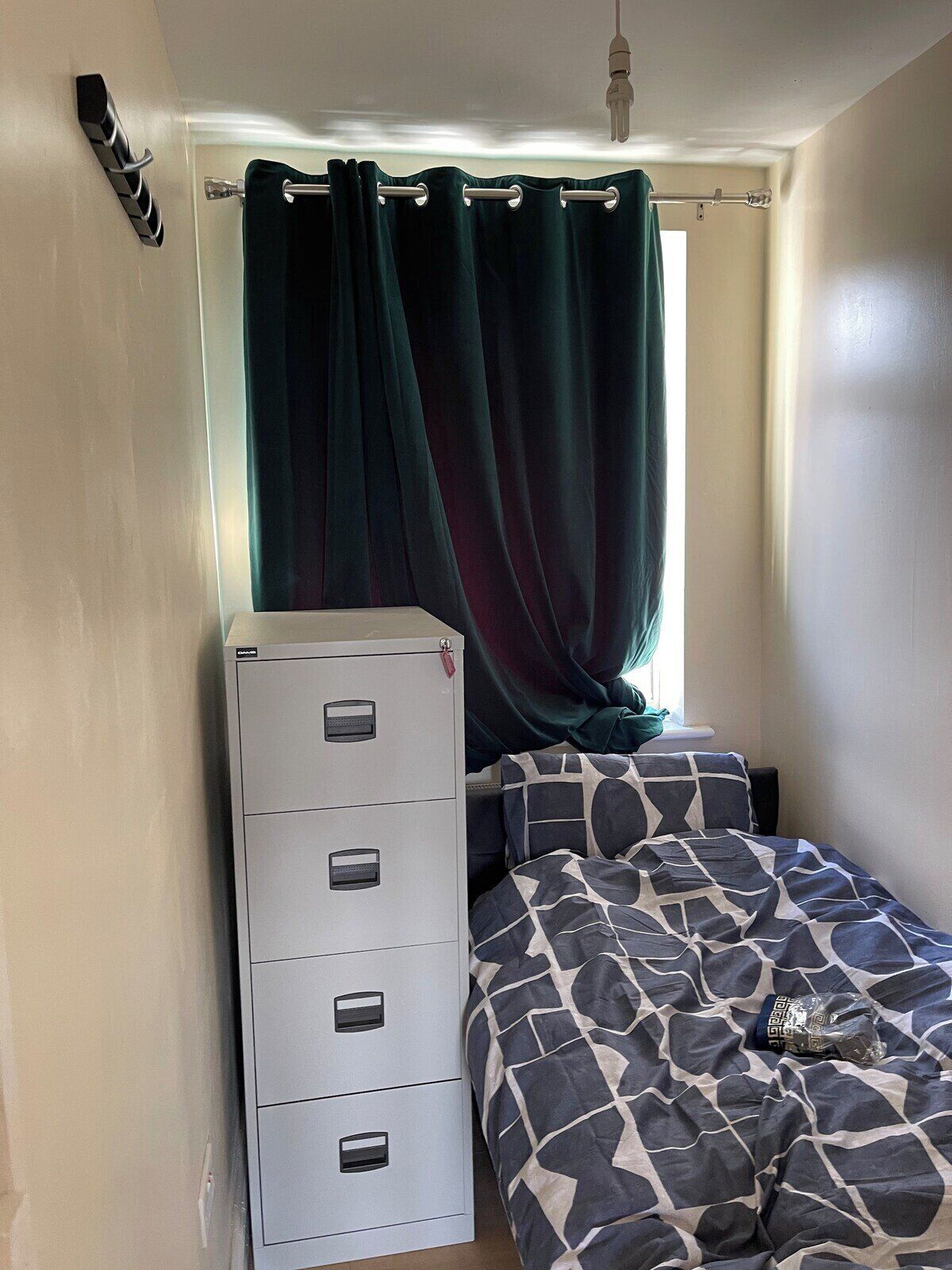A bedroom with a bed, a dresser, and a window with curtains.