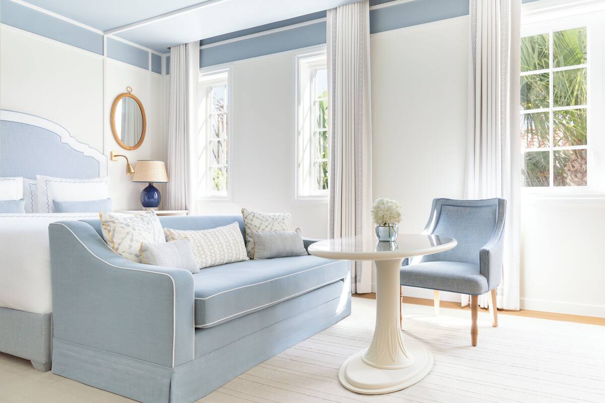 A bedroom with a bed, a blue sofa, a round table, and a chair.
