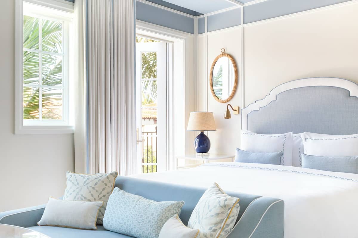 A bedroom with a bed, a nightstand, a lamp, a mirror, and a window with curtains.