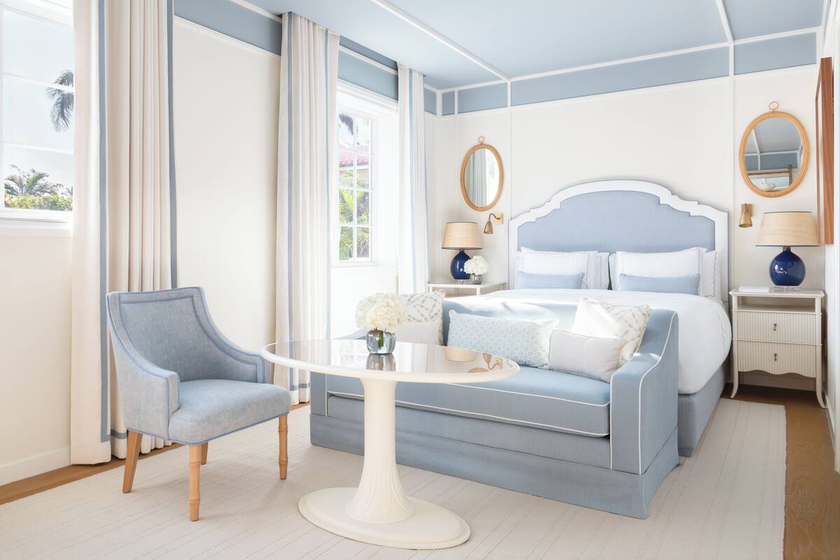 A bedroom with a bed, a chair, a table, and a nightstand.