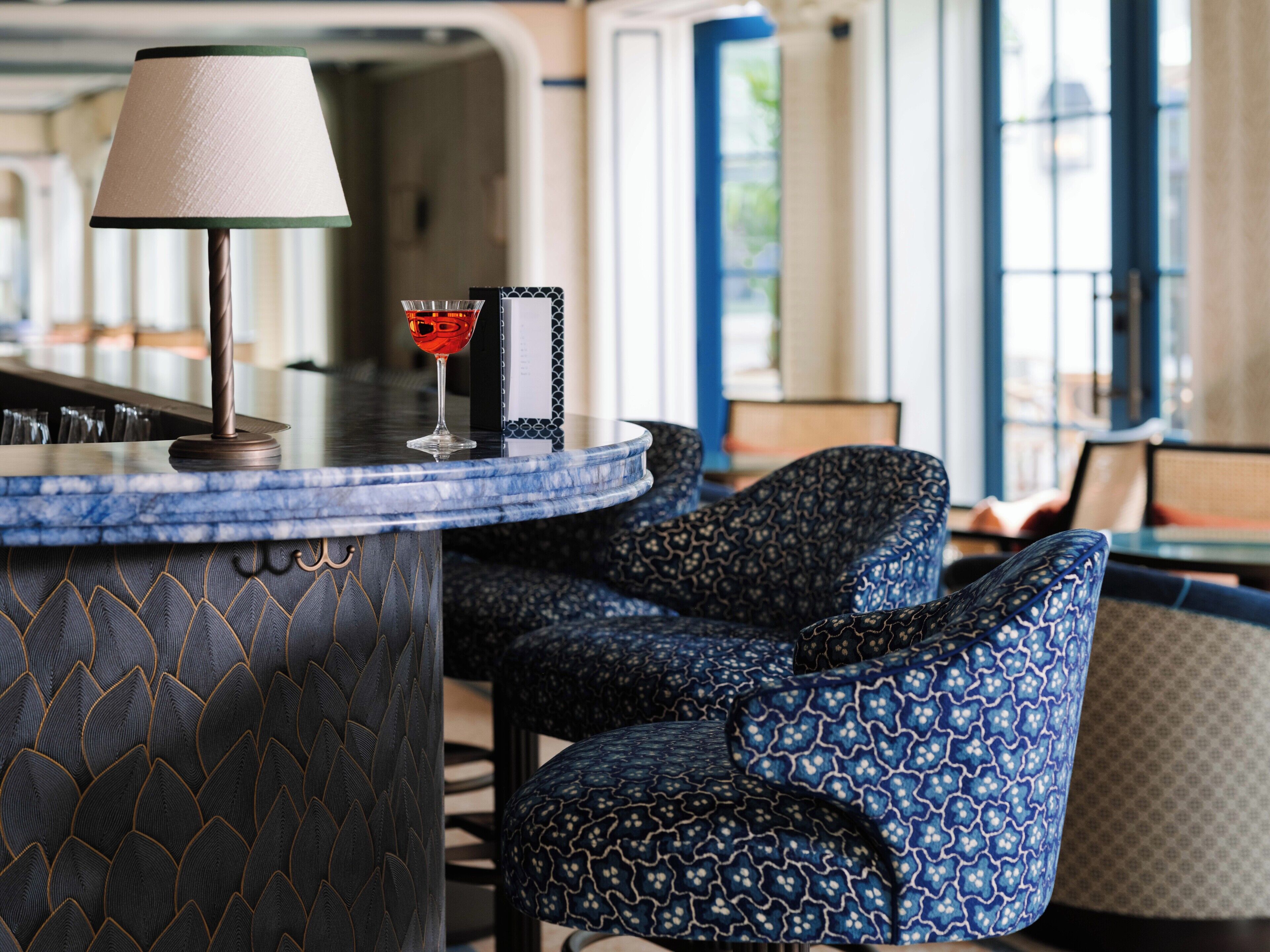 Un coin bar avec une lampe, un verre contenant un liquide rouge et des chaises à motifs.