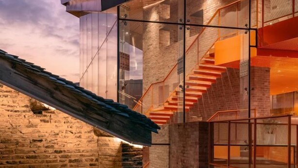 Ein modernes Gebäude mit Glasfassade, Backstein-Innenraum und einer Treppe mit orangefarbenen Geländern.