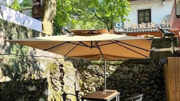 An outdoor patio with a table and chairs under a large umbrella, surrounded by stone walls and greenery.