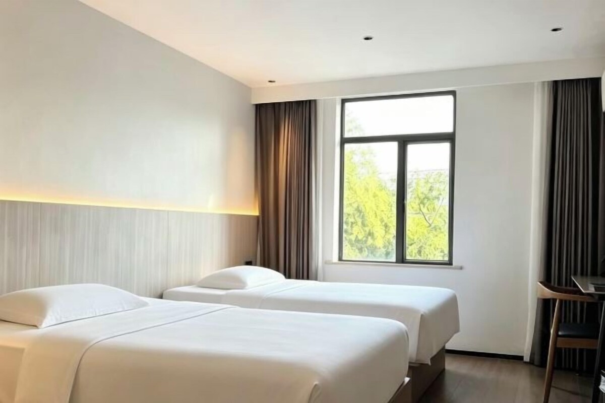 Een hotelkamer met twee bedden, een bureau en een raam met gordijnen.